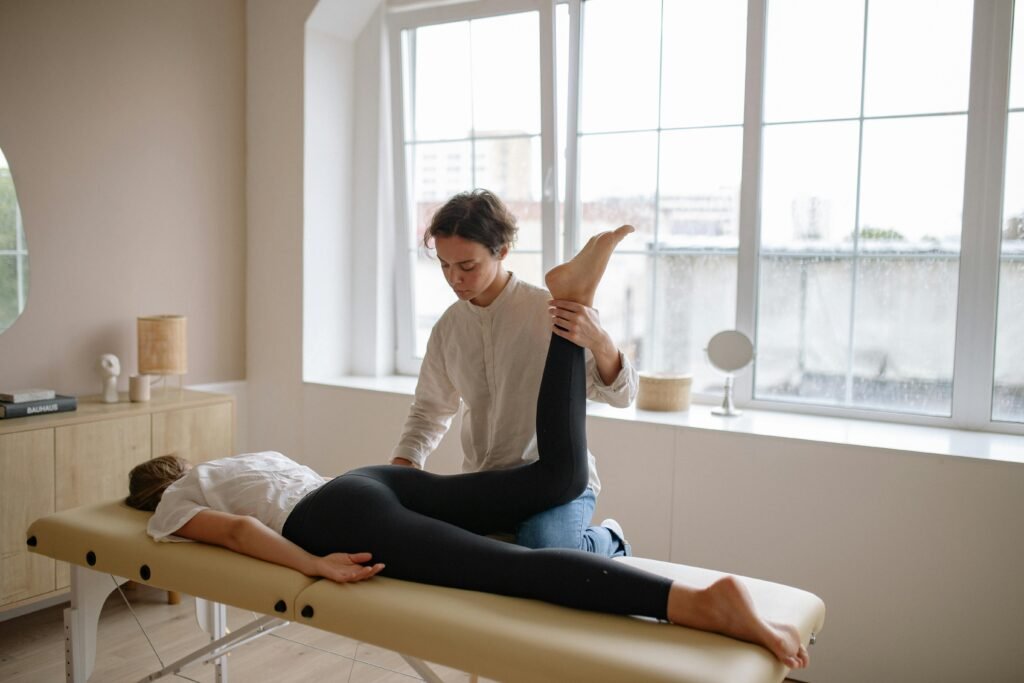 pexels-photo-5794011-5794011 Massage therapist provides leg therapy to client on a table in a sunlit room.