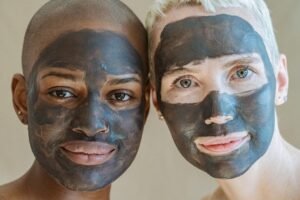 Crop positive diverse female friends with cosmetic masks on face looking at camera during spa procedures